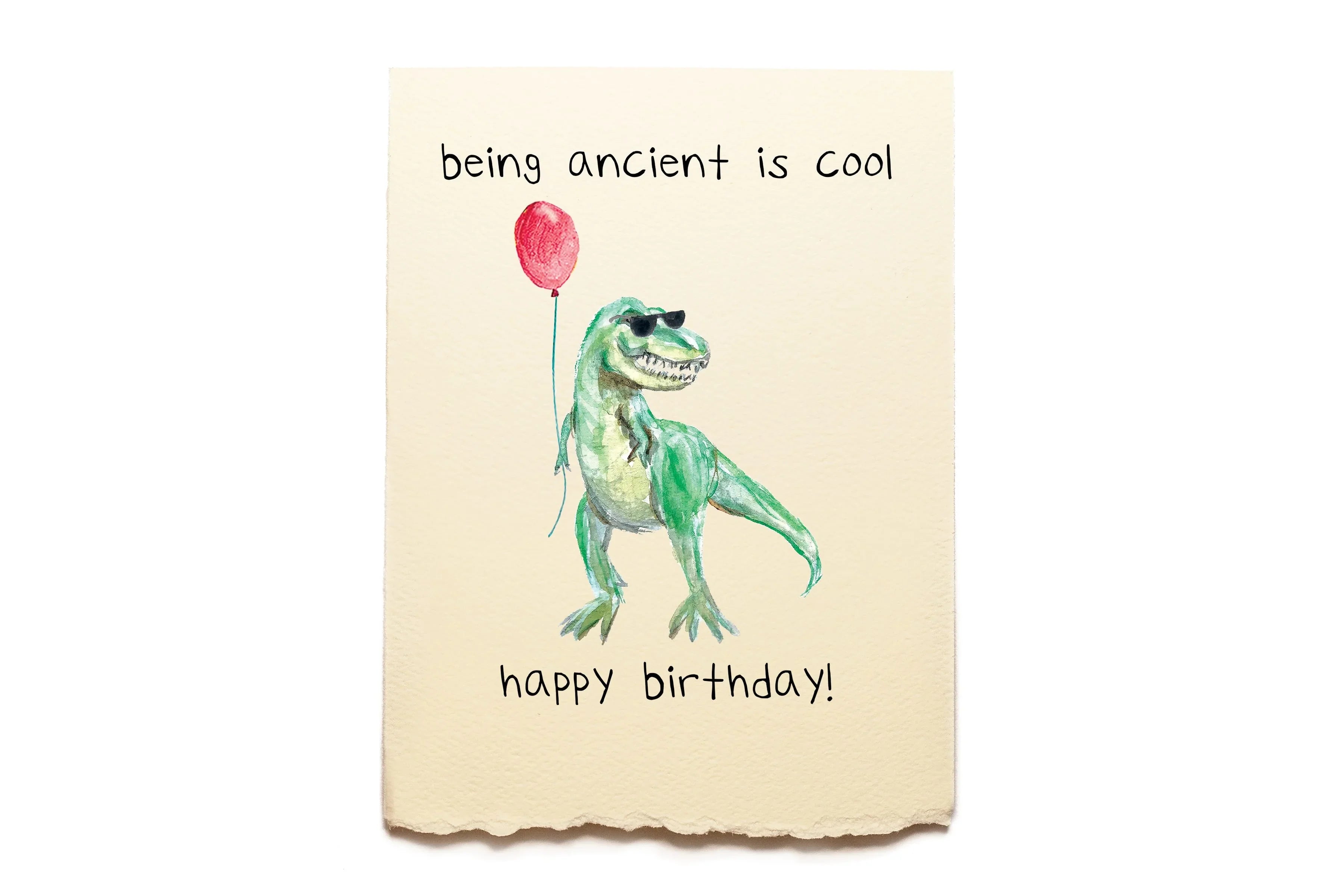 Dinosaur holding a red balloon with text 'being ancient is cool happy birthday!' on a beige background