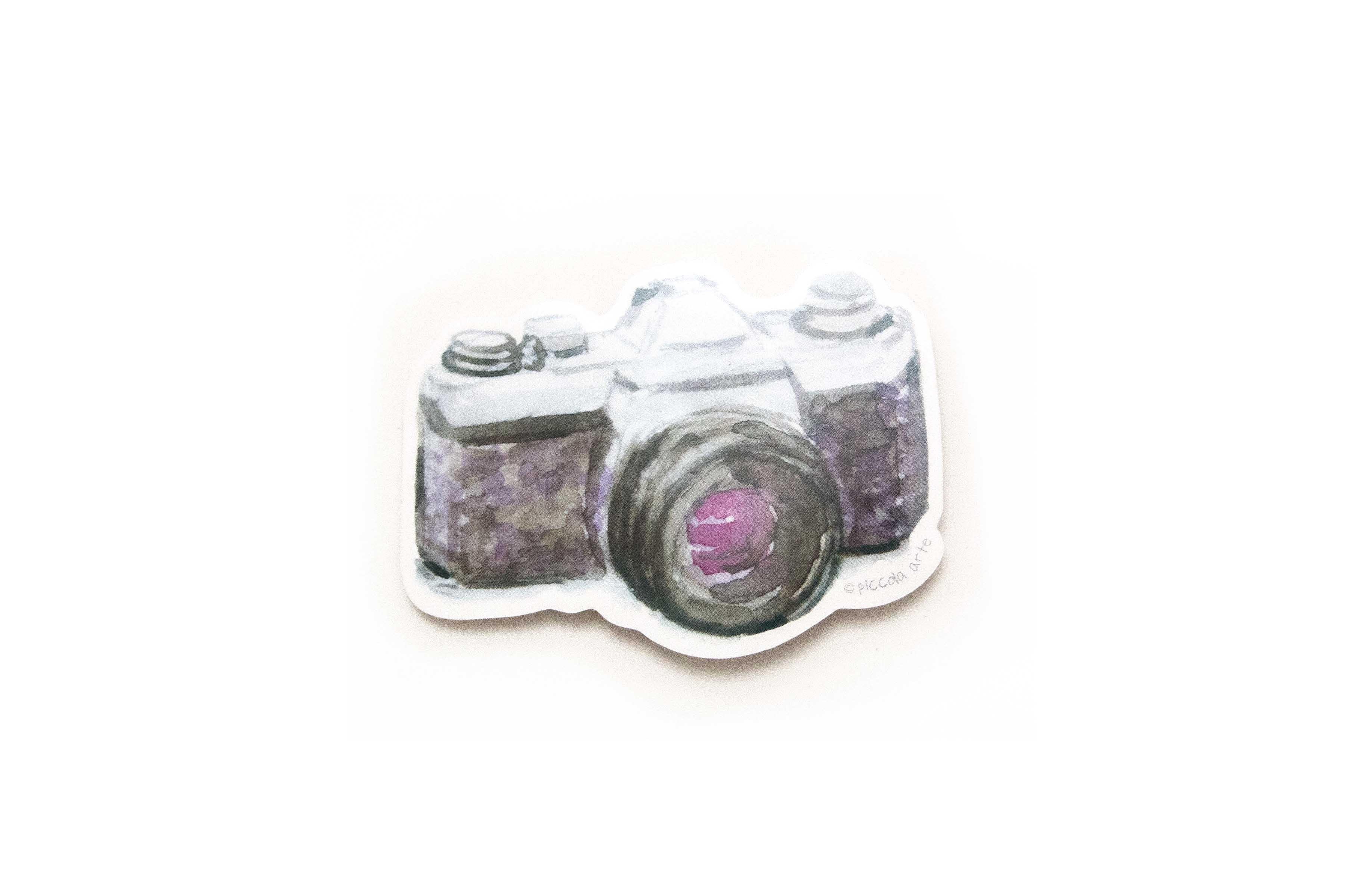 Camera-shaped charm with purple gemstones on a white background