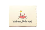 Newborn blanket with a cartoon crab and 'welcome, little one!' text on a beige background