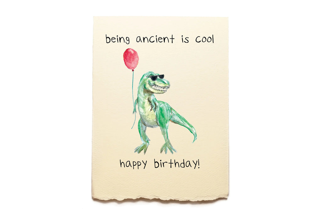 Dinosaur holding a red balloon with text 'being ancient is cool happy birthday!' on a beige background