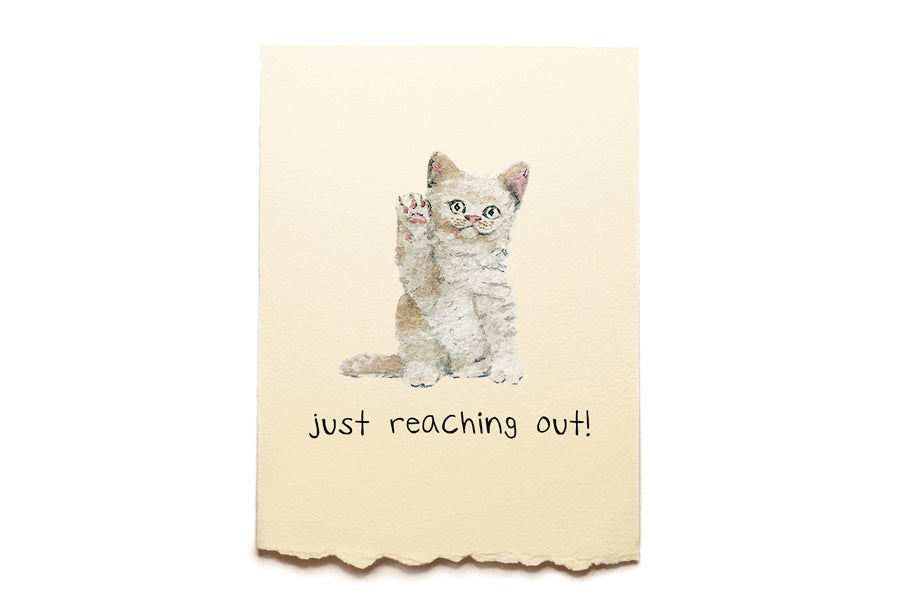 A greeting card with a kitten illustration and text 'just reaching out!' on a beige background