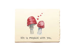 Card with red mushrooms and hearts on a beige background with text 'life is magical with you'.