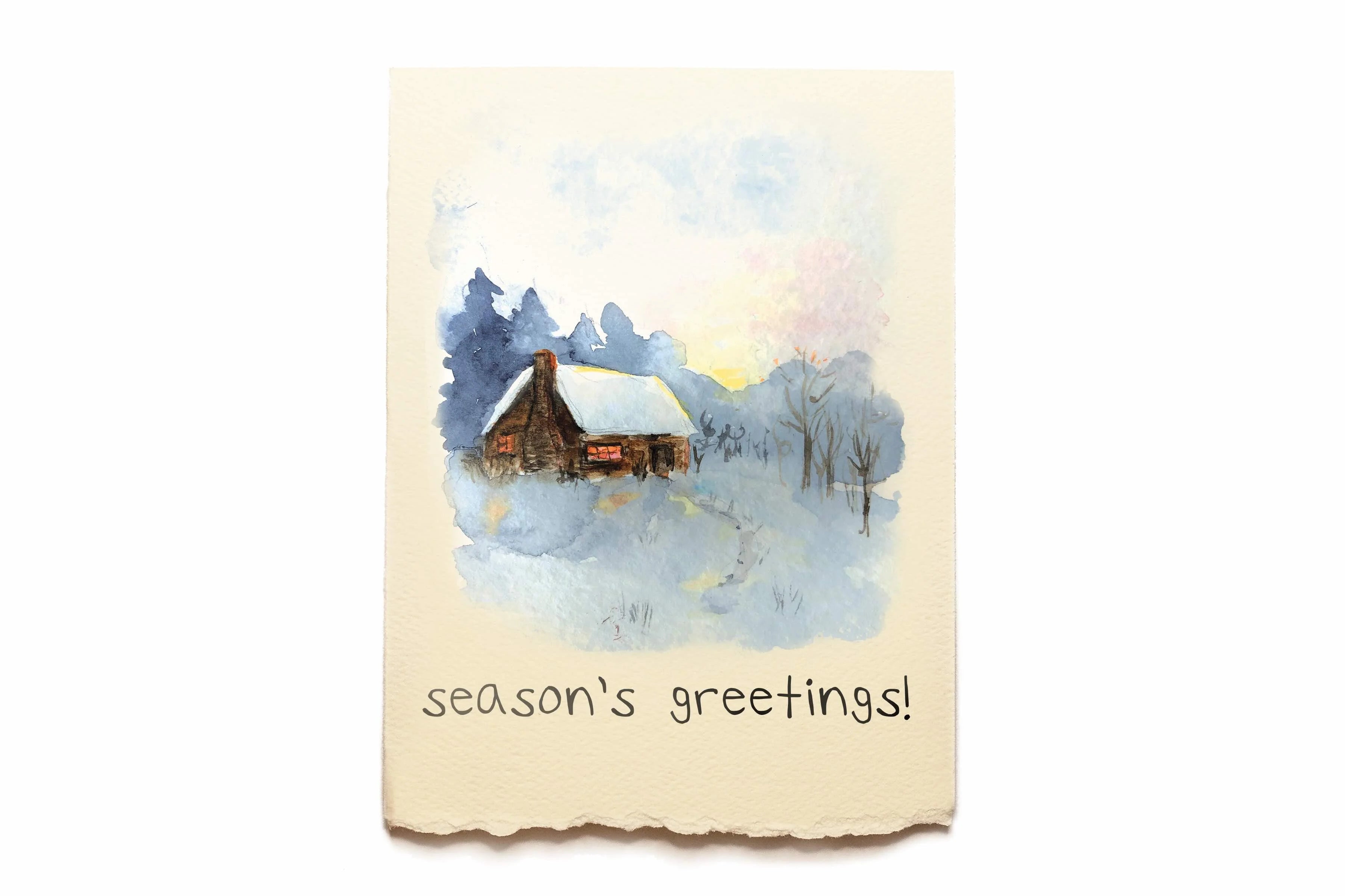 Greeting Card with a winter scene with a cabin and 'season's greetings!' text on a beige card.