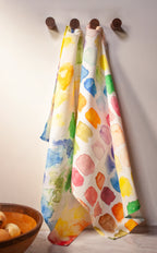 Colorful patterned towels hanging on wooden hooks against a plain wall.