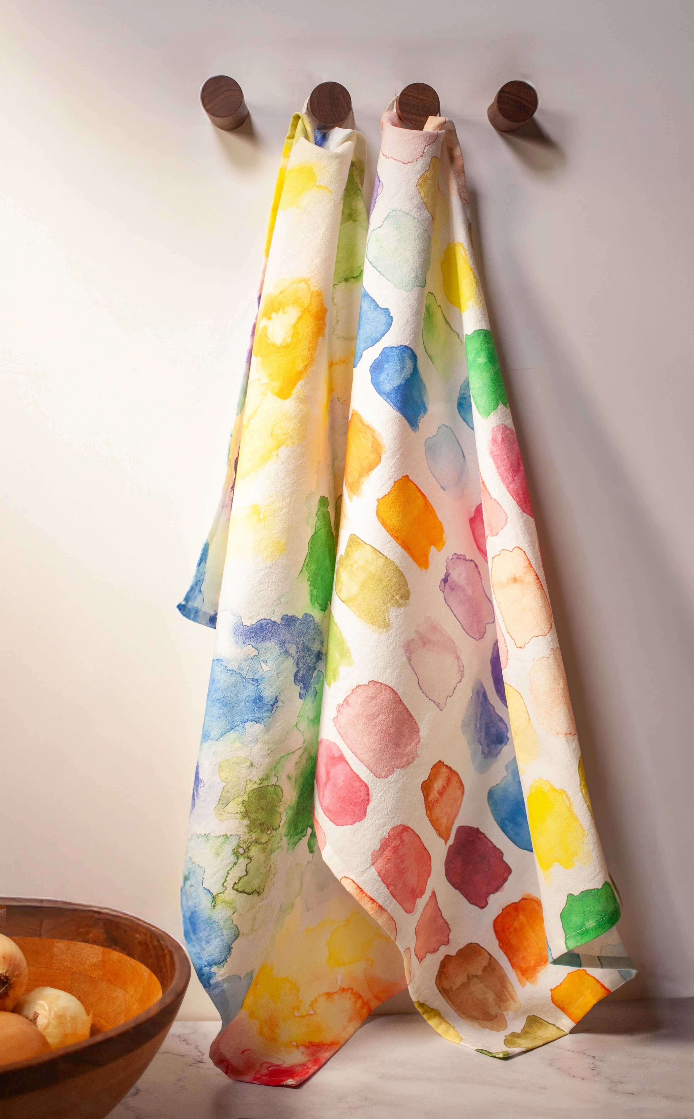 Colorful patterned towels hanging on wooden hooks against a plain wall.