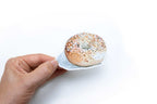 Hand holding a bagel with sesame seeds and cream cheese on a white background