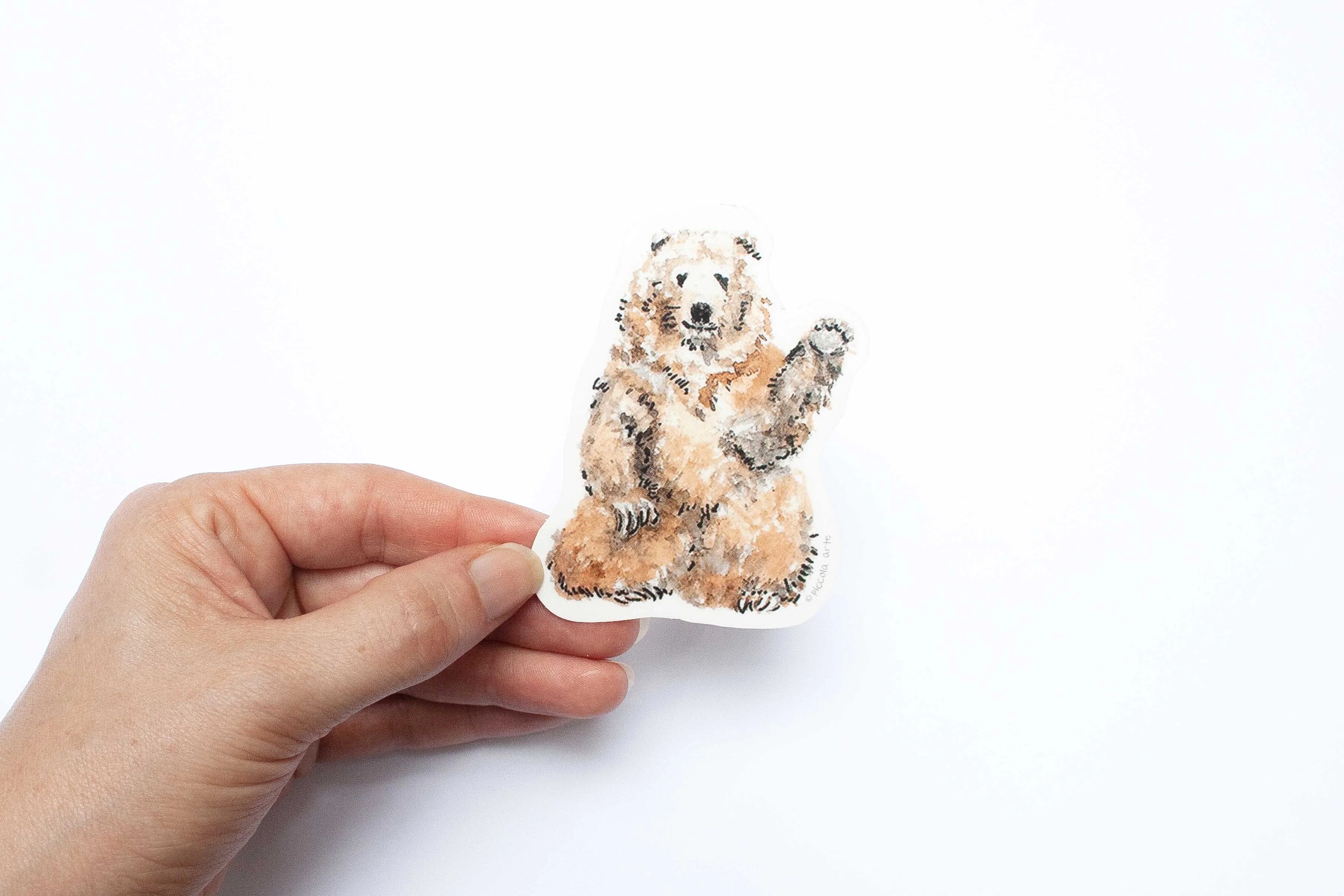 Hand holding a sticker cutout of a bear on a white background.