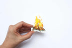 Hand holding a sticker cutout of a campfire with flames on a white background.