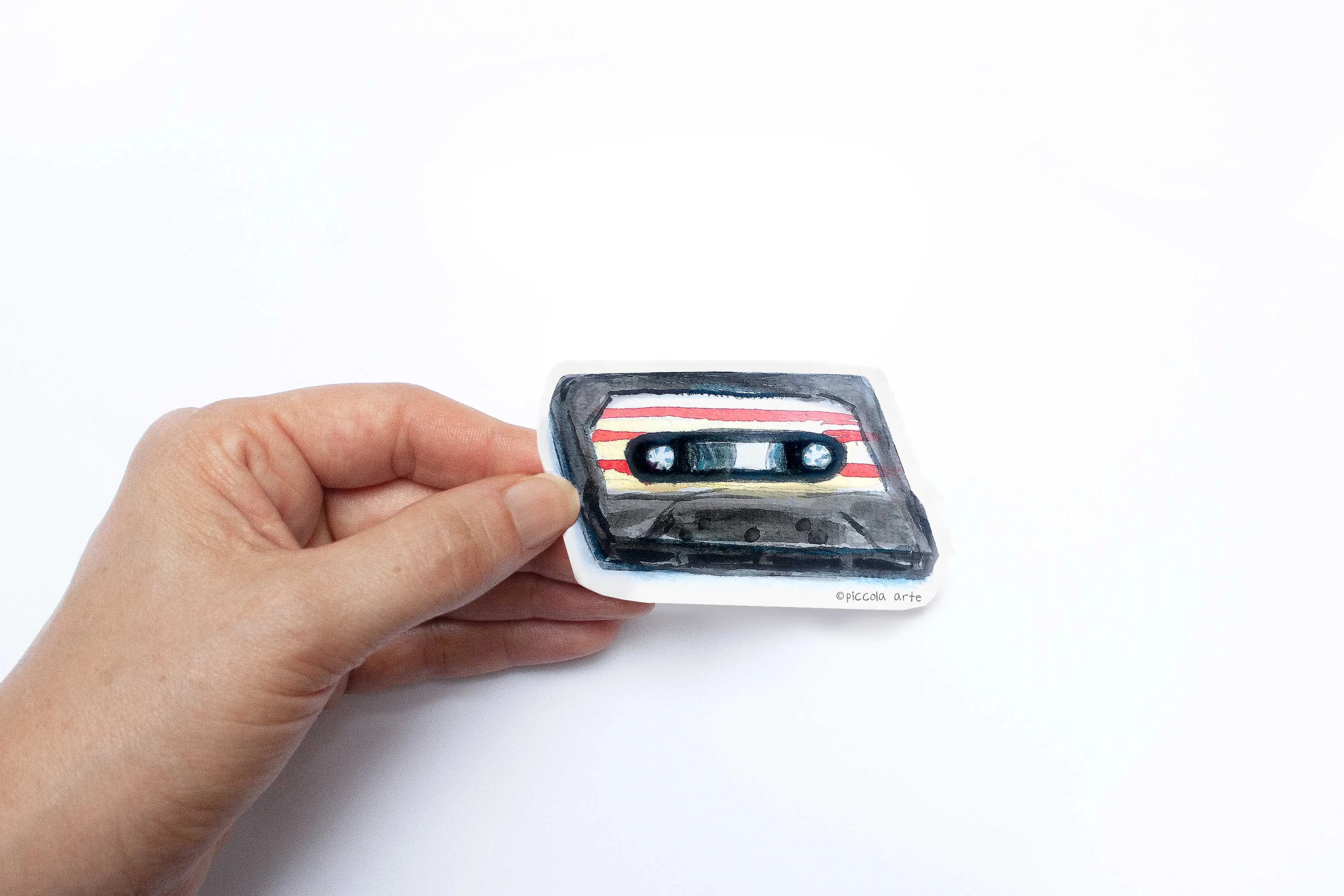 Hand holding a small cassette tape on a white background