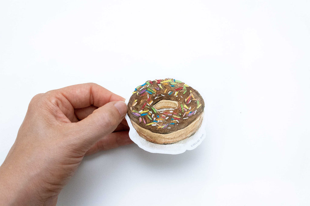 Hand holding a small donut-shaped object with sprinkles on a white background