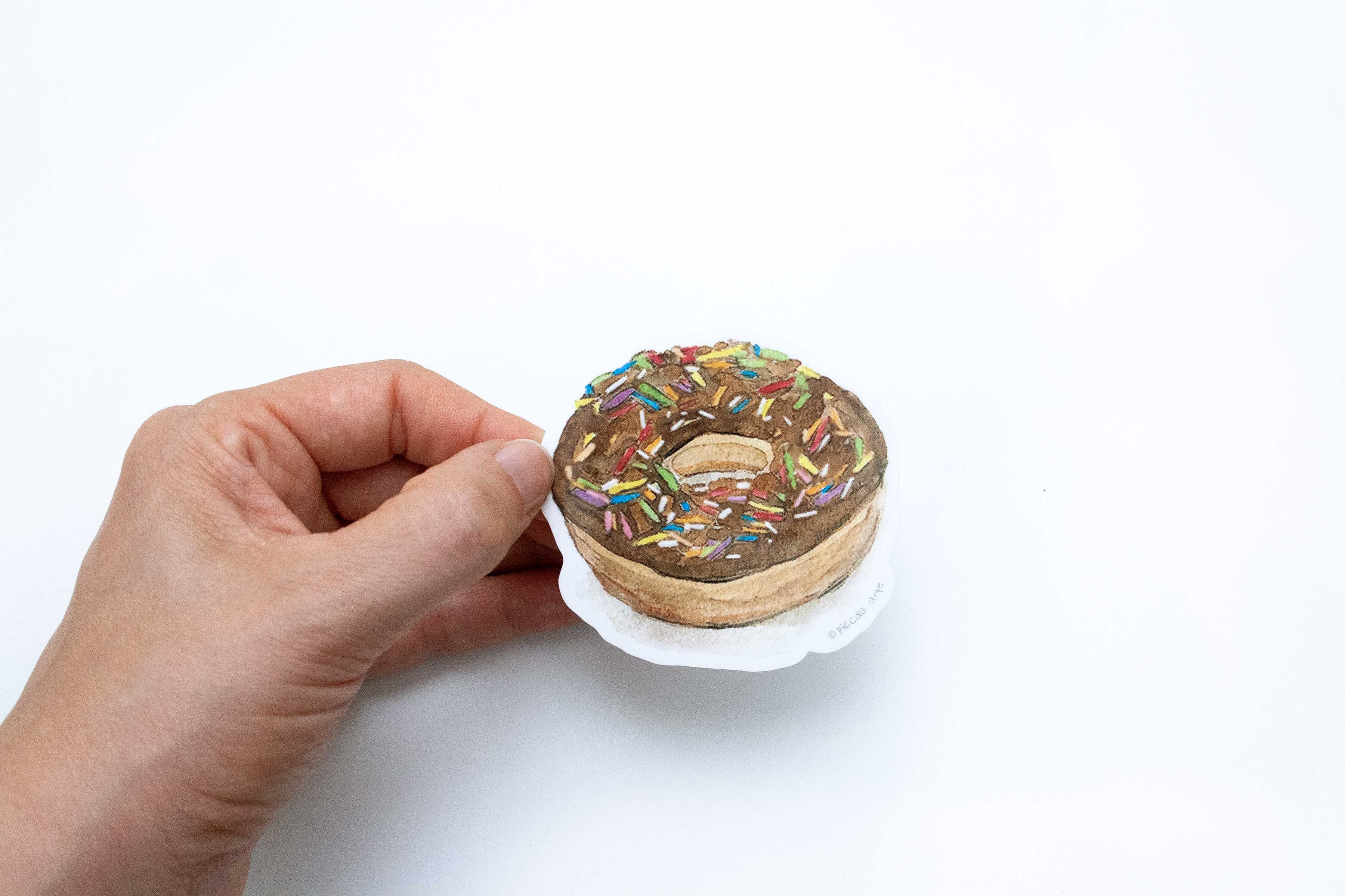 Hand holding a small donut-shaped object with sprinkles on a white background