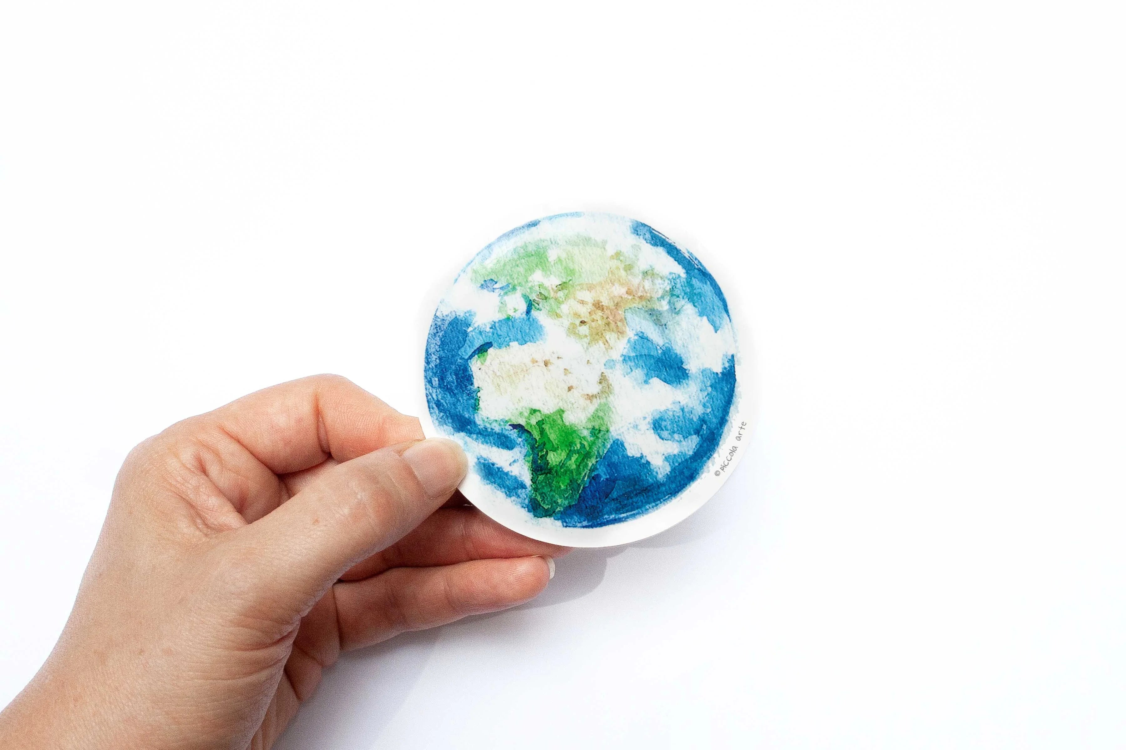 Hand holding a small round sticker of mother earth design on a white background.
