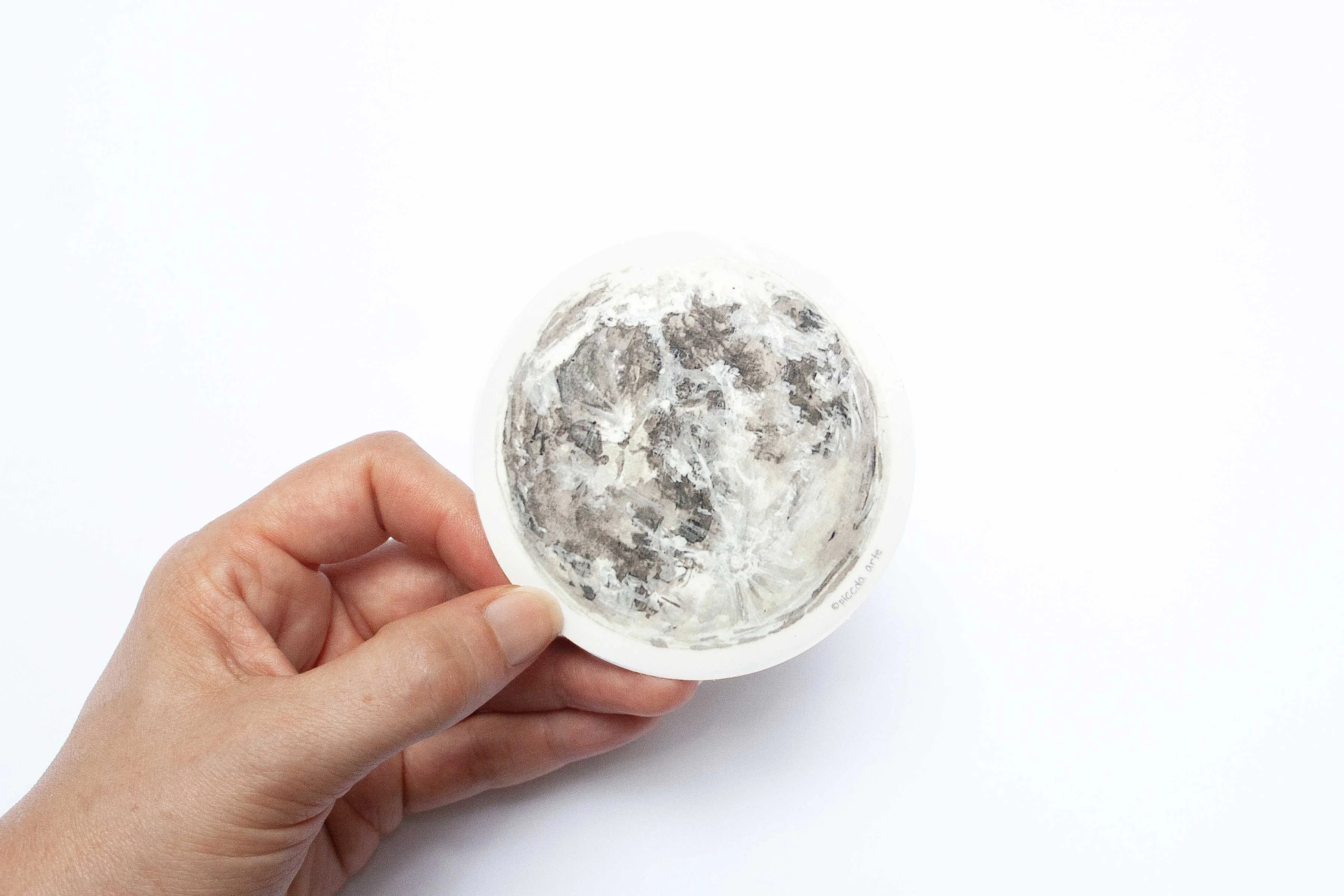 Hand holding a moon sticker on a white background.