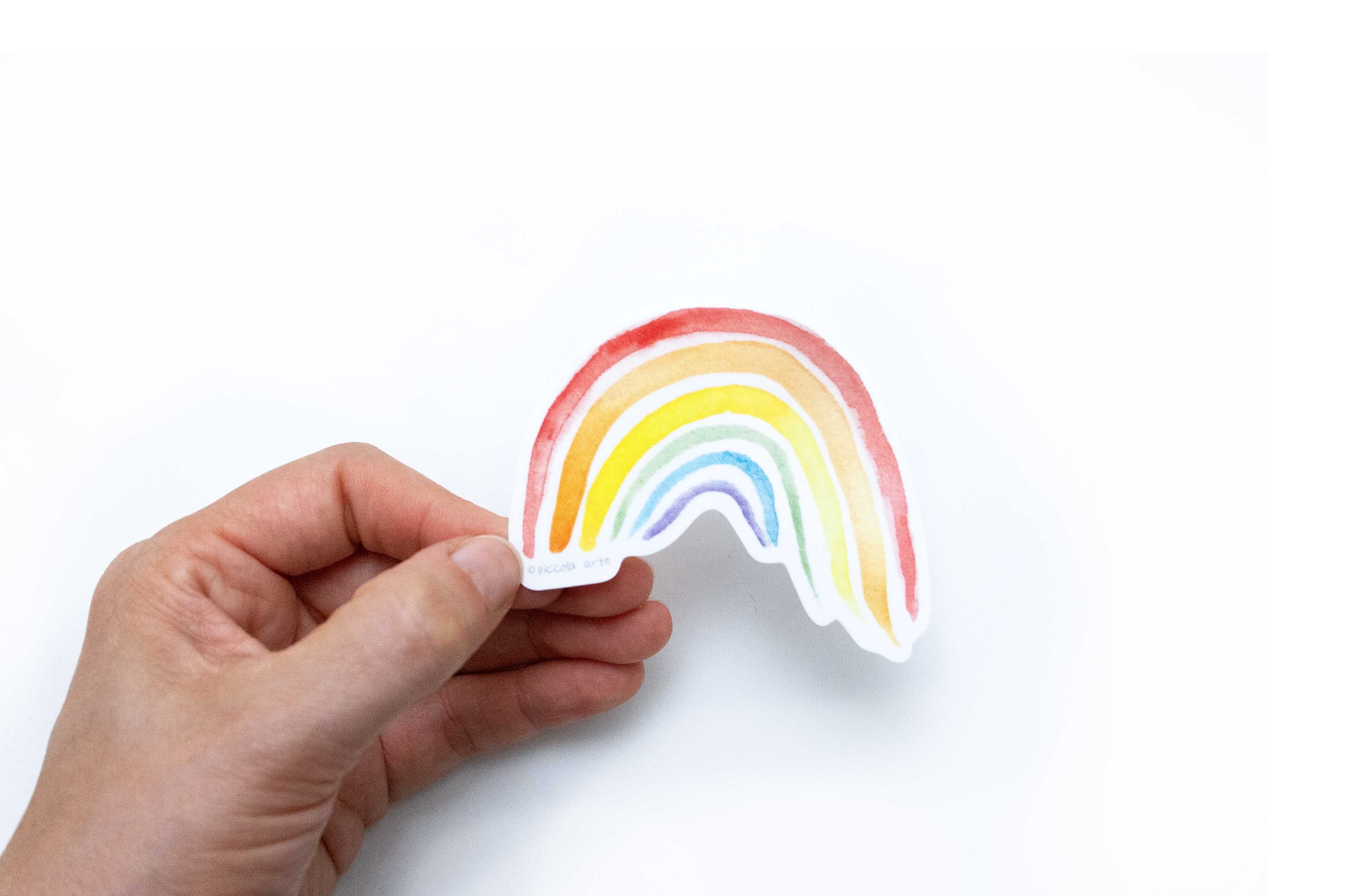 Hand holding a colorful rainbow sticker against a white background