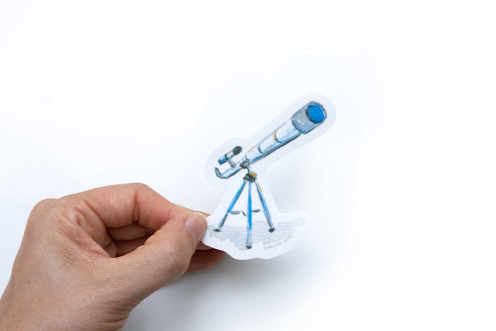 Hand holding a paper cutout of a telescope on a white background