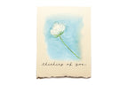 Card with a white flower illustration and 'thinking of you' text on a blue watercolor background.