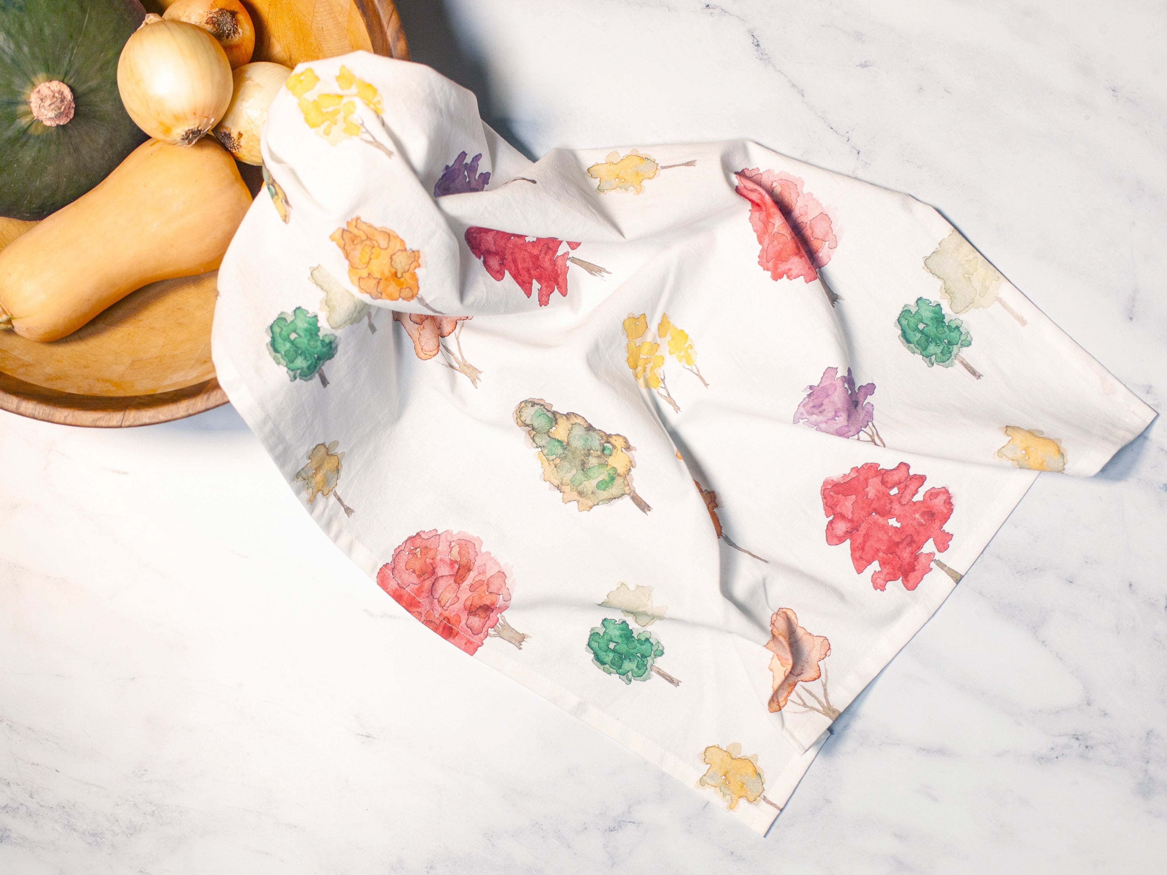 Two folded fabric swatches with colorful leaf patterns on a marble surface.