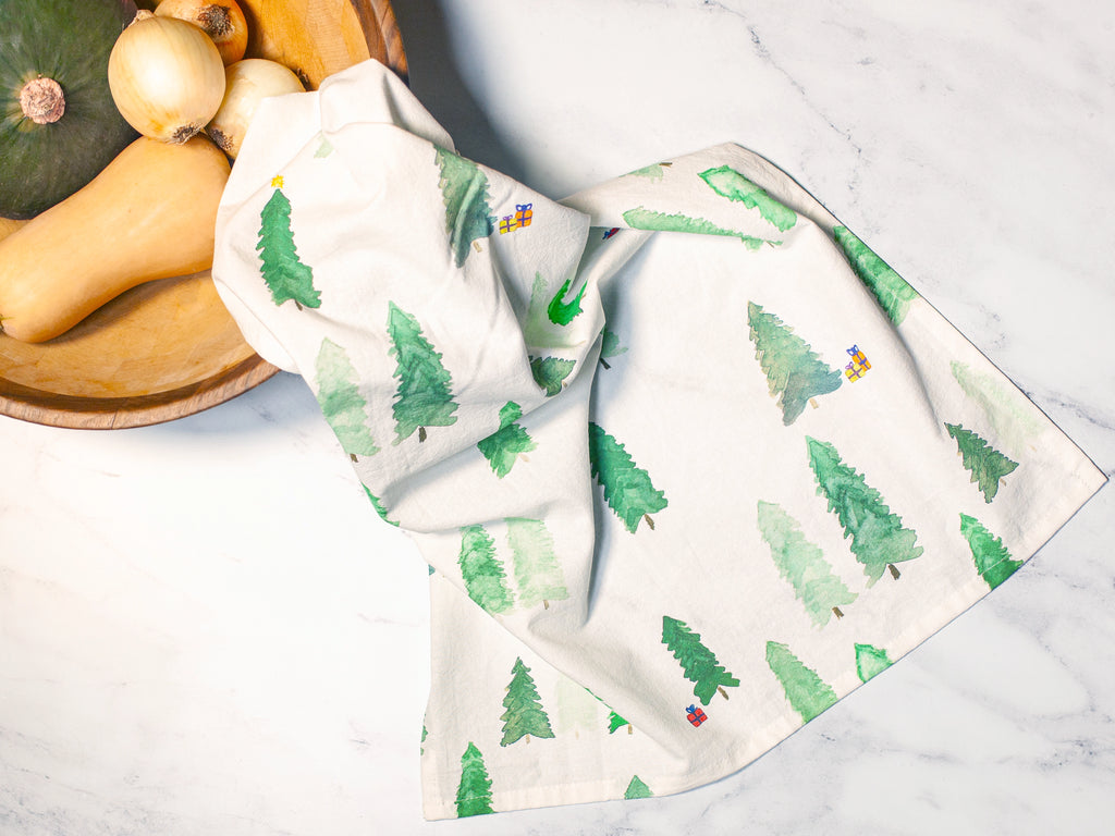 Two kitchen towels with tree pattern on a marble surface with vegetables.