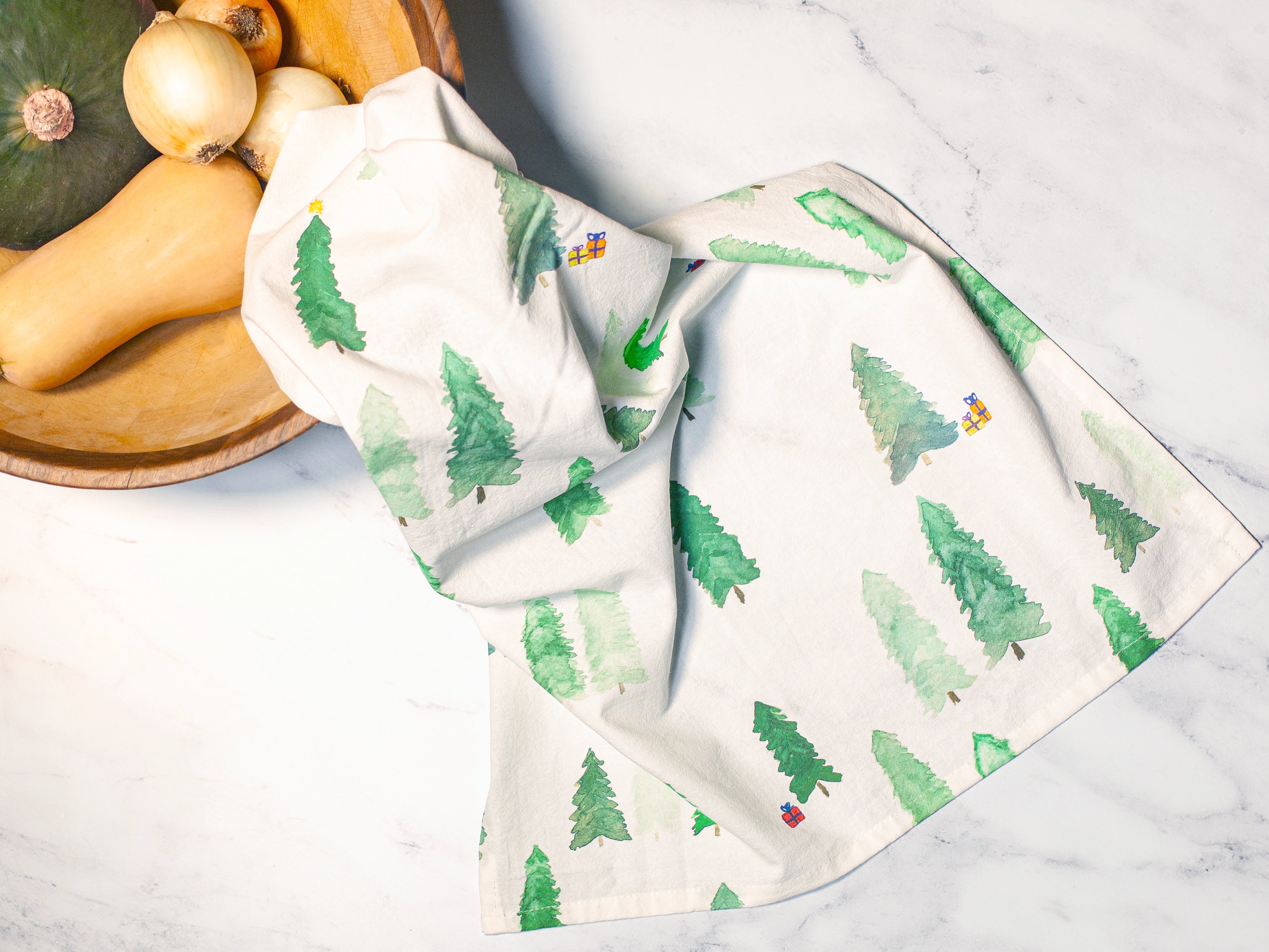 Two kitchen towels with tree pattern on a marble surface with vegetables.