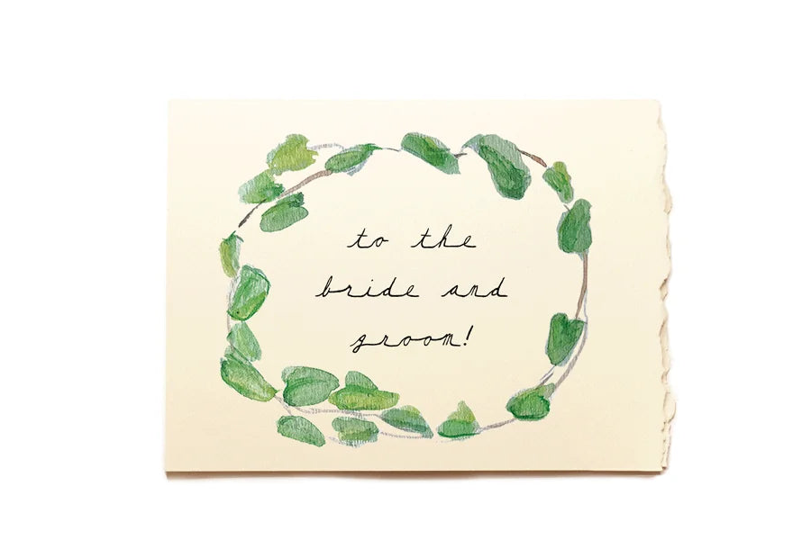 Greeting card with green leaf wreath and text 'to the bride and groom' on a beige background